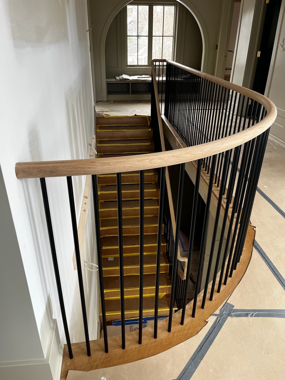 Curved wood handrail updated with slender black iron balusters