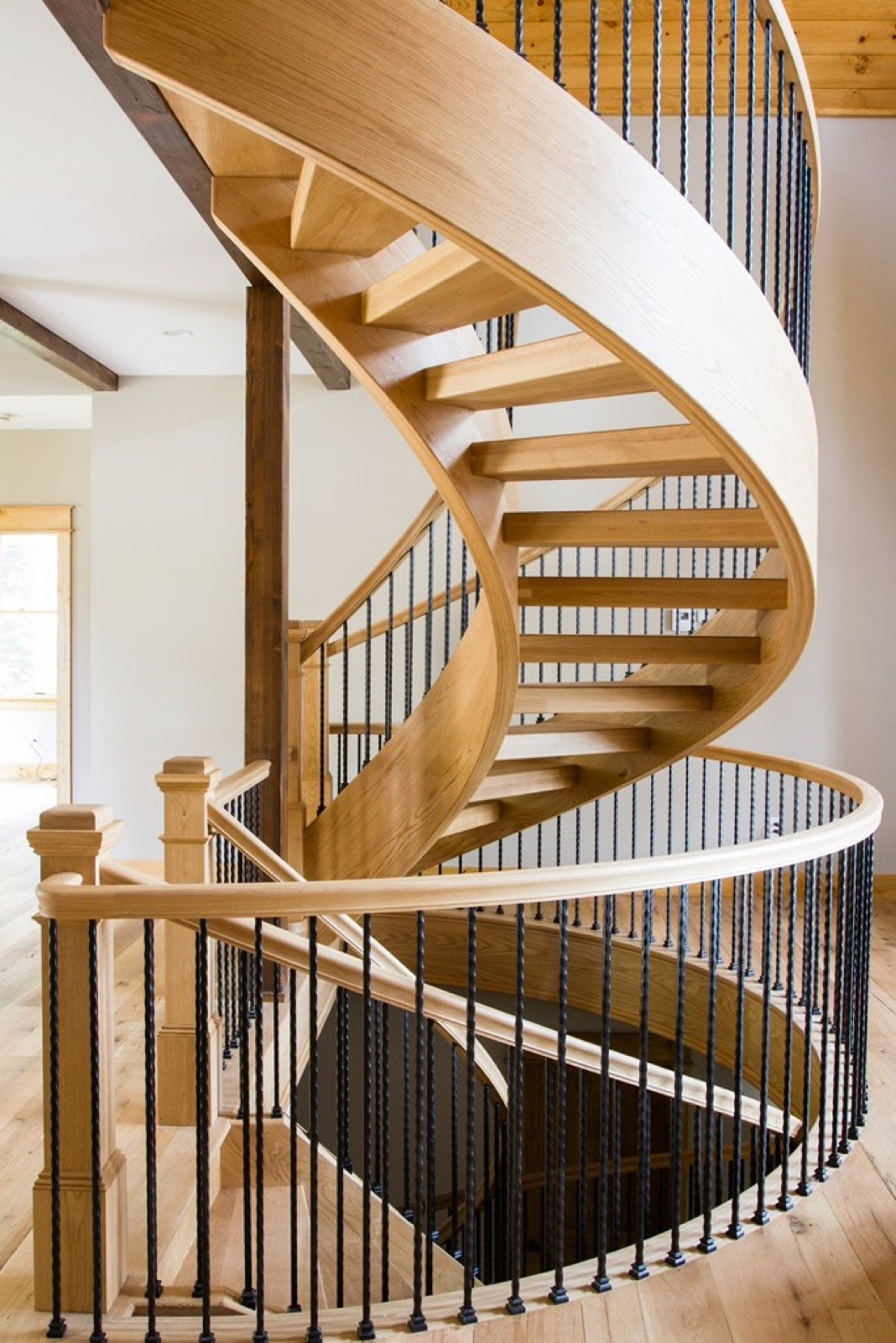 Sculptural curved staircase with white oak handrail and slim black balusters
